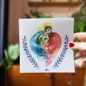 Kwadratowa kartka z rysunkiem Świętej Rodziny. Otaczają ją gałązki niebieskich gałęzi.