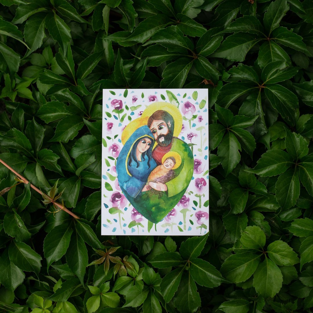 Miniplakat z akwarelowym wizerunkiem Świętej Rodziny. Maryja i Józef przytulają razem małego Jezusa. Otaczają ich kwiaty.
