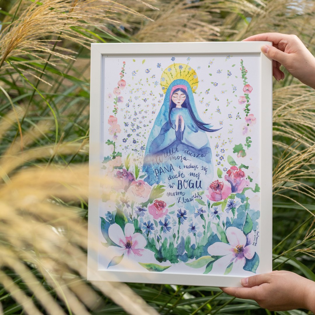 Plakat z modlącą się Maryją. Otaczają ją kwiaty na łące. Oprawiony w białą ramę.