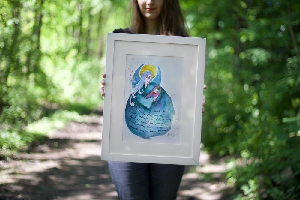 Plakat z niebieskim aniołem przytulającym dziecko i modlitwą do Anioła Stróża. Oprawiony w białe passe-parotut i białą prostą ramę.